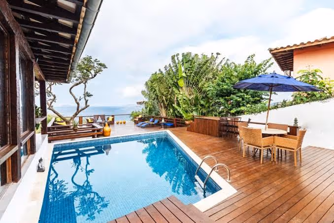 Deck de madera con sombrilla azul y mesa frente a la piscina